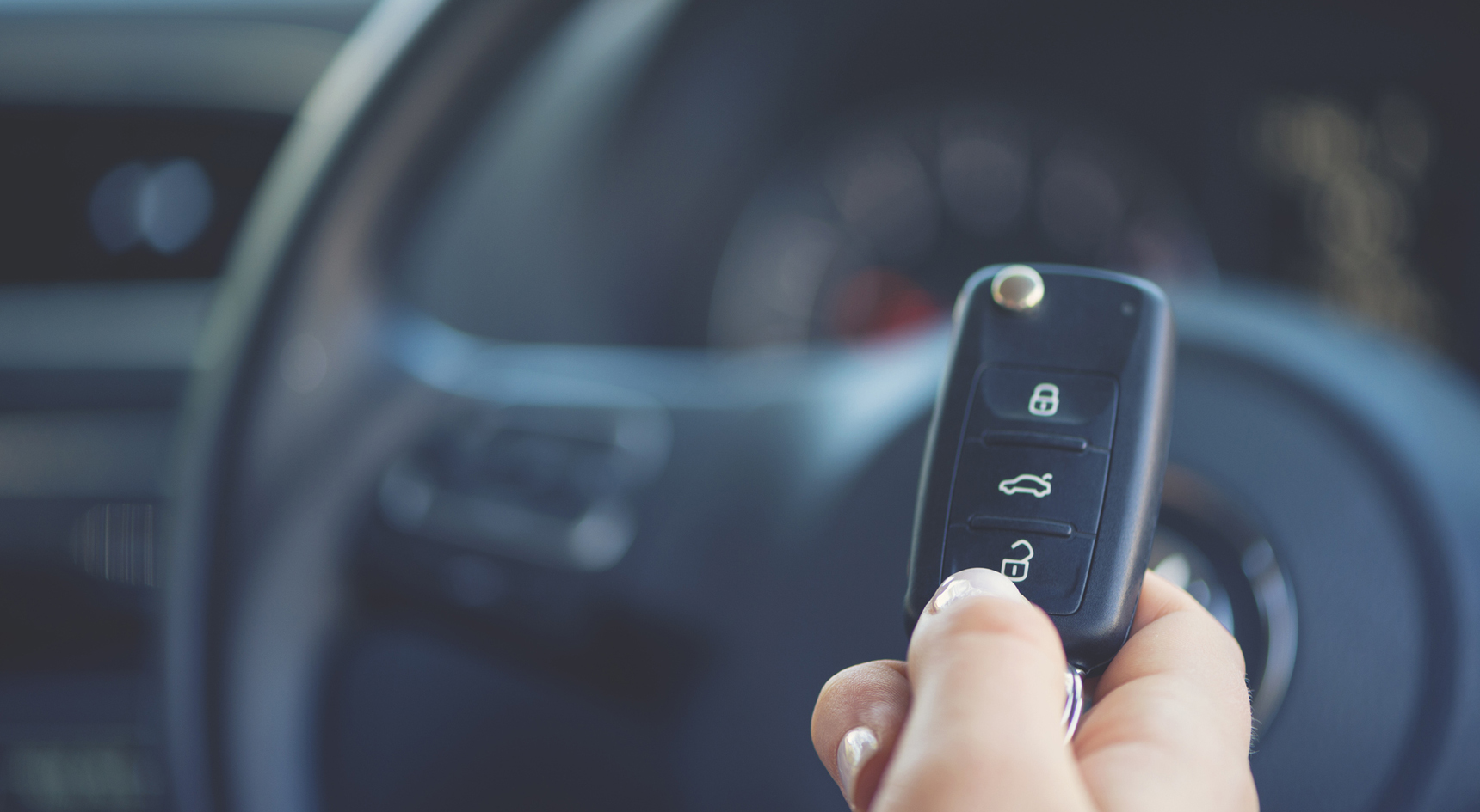 A person's hand with a pair of keys and a steering wheel in the background.
