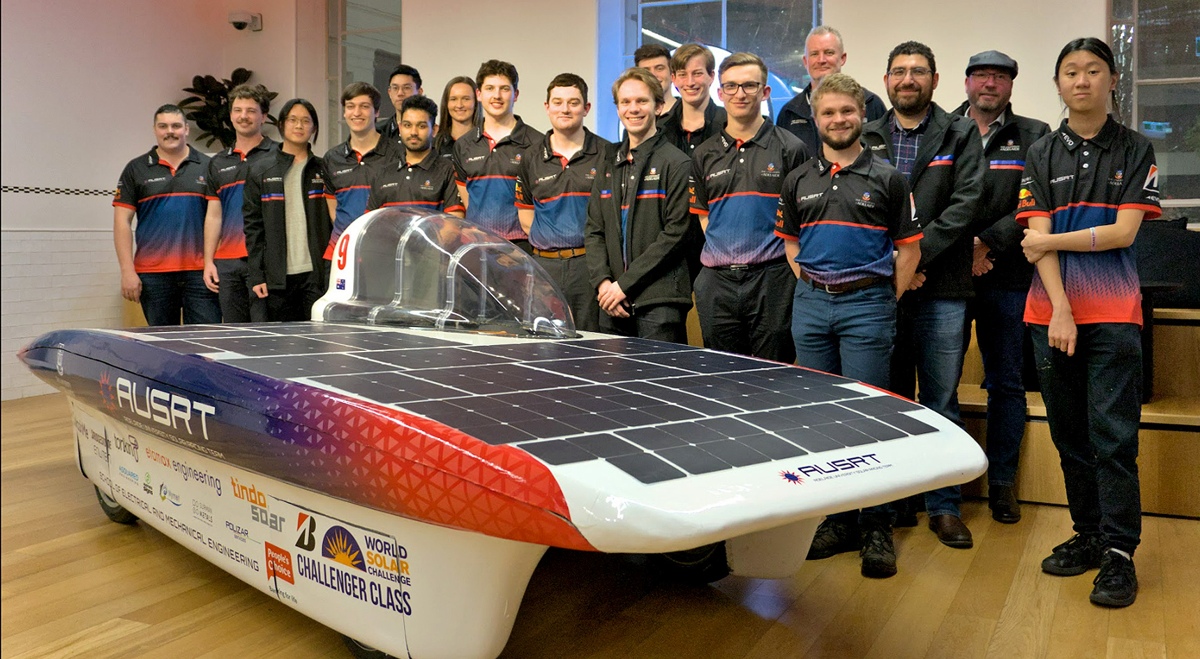 A group of university students standing around a futuristic looking car.