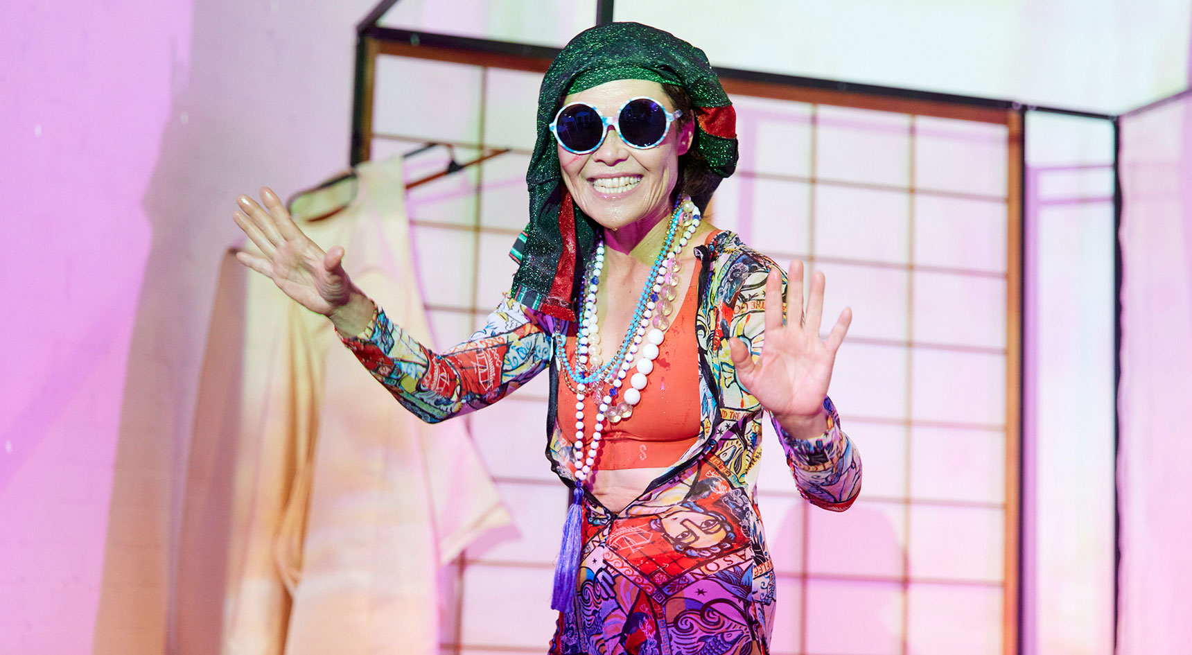 A woman dressed very vibrantly with big round sunglasses and a big smile