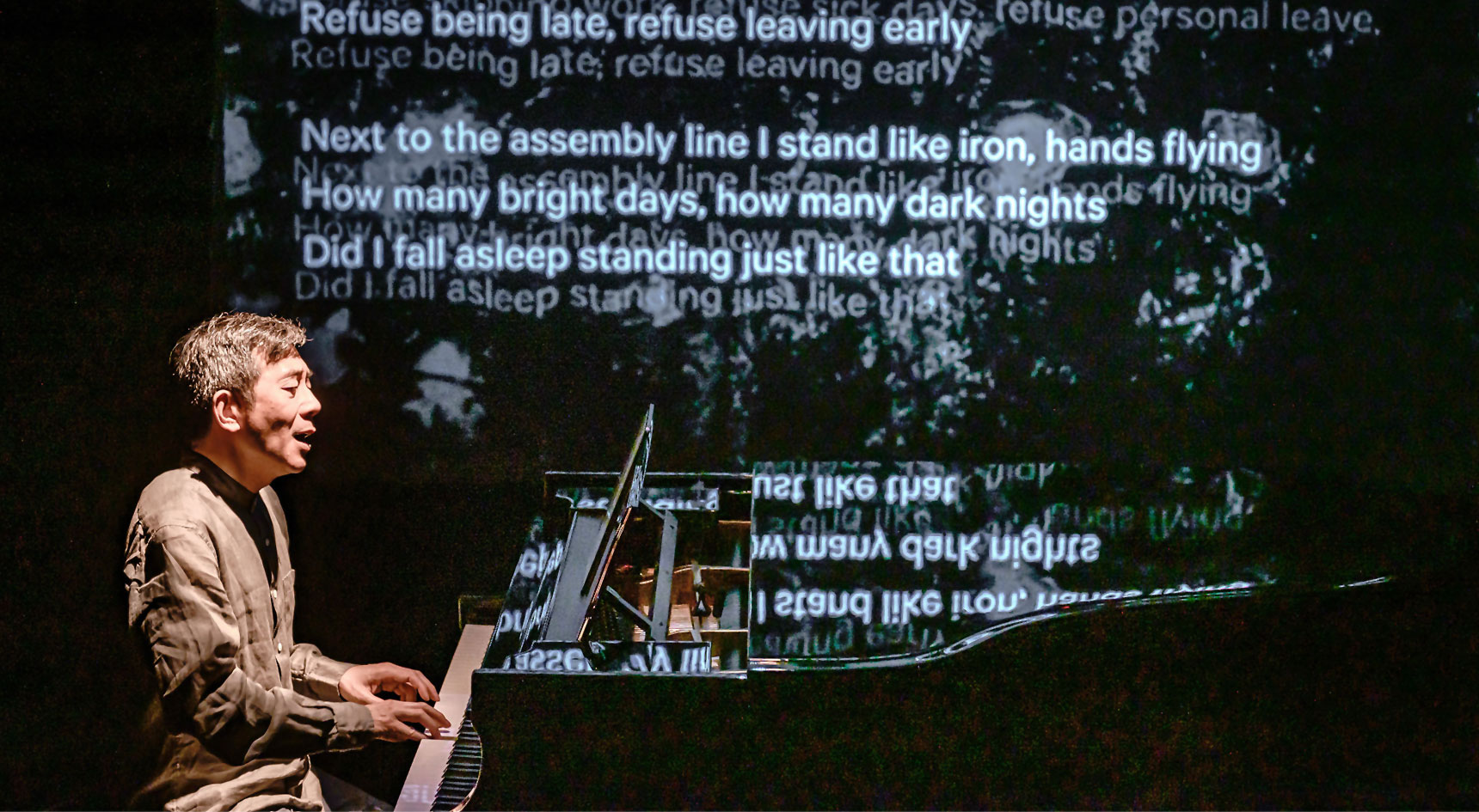 A man at a piano with a screen of poetry behind