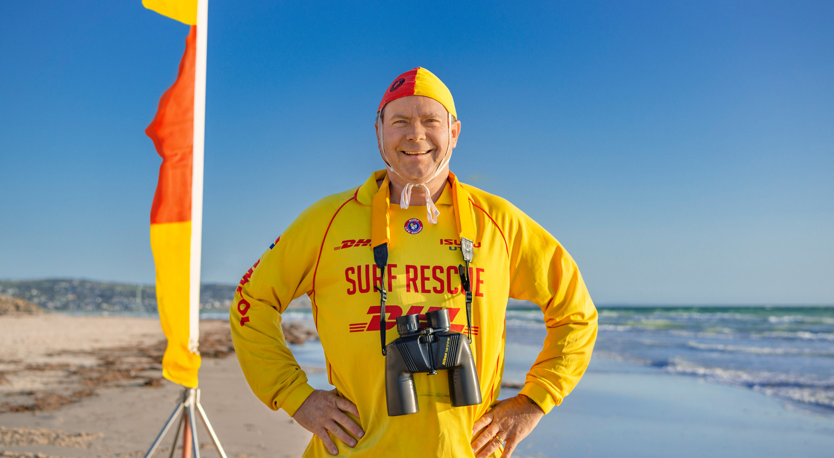 Darren standing on the beach in front of the yellow and red flags.