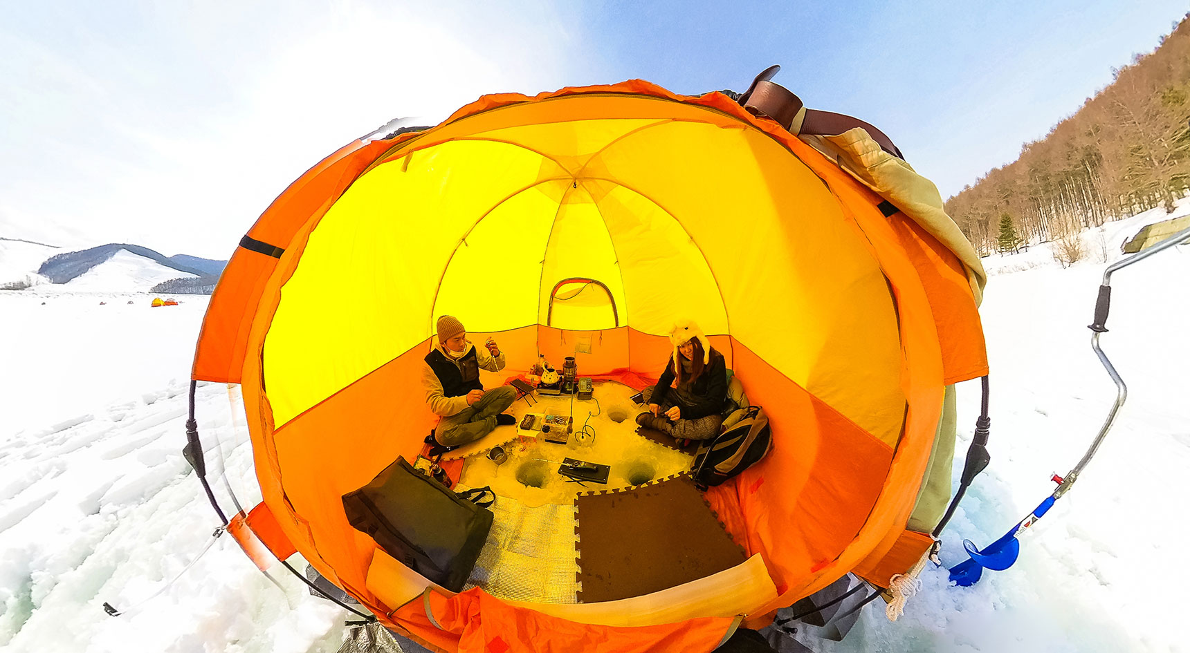 People sitting in a tent fishing through ice.